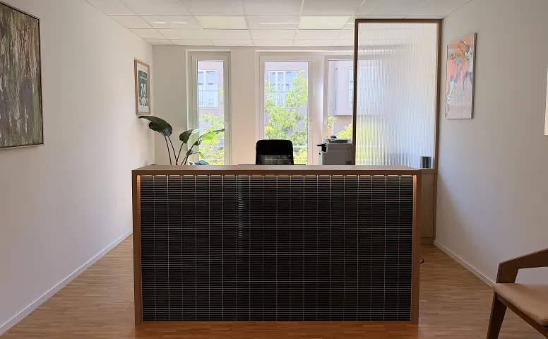 Custom reception counter in dark timber and tile against a reeded-glass partition, Munich